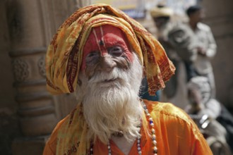 Old Hare Krishna follower dressed in orange dress in front of temple in Govardhan, India, Asia