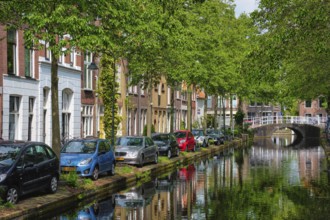 Delft, Netherlands, May 12, 2017: Cars and bicycles parked on canal embankment in street of Delft