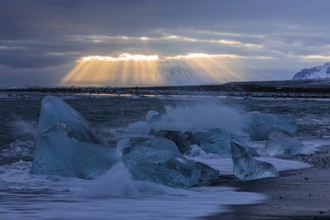 Waves breaking on icebergs on the black beach of Breidamerkursandur, sunset, near Jökullsarlon,