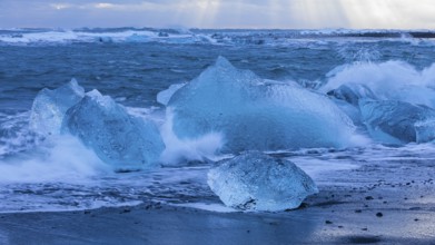 Waves breaking on icebergs on the black beach of Breidamerkursandur, near Jökullsarlon, Sudurland,