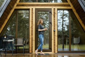 Barefoot woman came out on the wet terrace of a triangular summer house after the rain with a cup