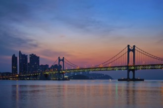 Gwangan Bridge on sunrise with skyscrapers and dramatic sky. Busan, South Korea, Asia