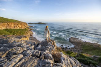 Young woman standing on a rock above the sea in the evening light, beach at The Gap, Robberg