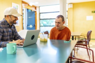 Cauasian adult man with disability and colleague working in the cafeteria of coworking
