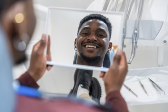 Happy patient looking at his whiter teeth in the mirror at the dental clinic after a whitening