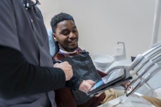 Dentist showing a dental x ray on a tablet to a smiling patient during a consultation in a modern