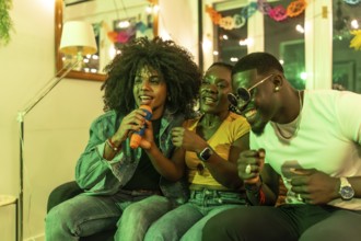 Man singing karaoke sitting on sofa with multi-ethnic friends at night