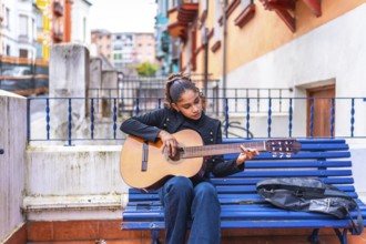 African american beauty woman playing acoustic guitar sitting in a blue bench in the city