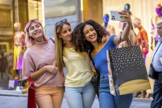 Three multi-ethnic diverse young women taking selfie carrying shopping bags in a mall