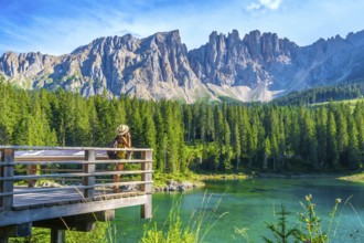Female tourist admiring the stunning landscape of lake carezza with the latemar massif in the