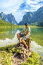 Tourist enjoying the scenic view of lake dobbiaco and the dolomites mountains while sitting on a