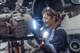 Skilled female mechanic wearing safety glasses and earplugs, meticulously inspecting a gearbox in a