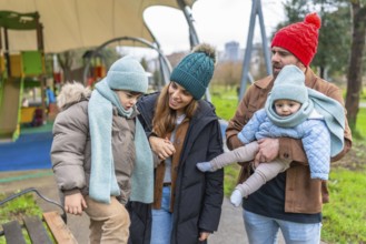 Happy family with two children having fun together at the playground during a cold winter day