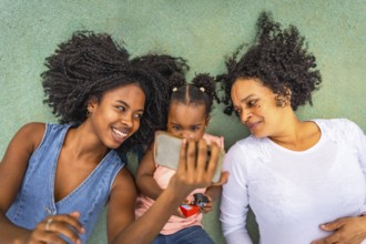 Top view of three african multi-generation woman watching the screen of the mobile lying down in a