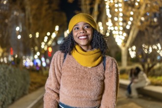 Portrait of a young black woman wearing winter clothes, smiling in a christmas decorated city at