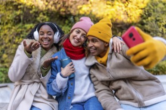 Three cheerful friends are taking a selfie in a city park, enjoying a winter day together