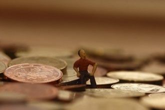 Miniature man sitting among euro coins, North Rhine-Westphalia, Germany, Europe