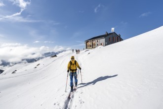 Ski tourers in front of the Chamanna d'Es-cha mountain hut in a wintry mountain landscape, Bündner