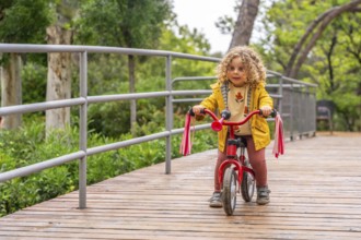 Adorable girl riding a pink bicycle along a park bridge in a spring day