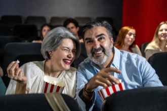 Mature couple having fun watching a comedy film at the movie theater, sharing popcorn and laughing
