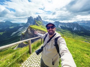 Photographer with backpack and camera taking a selfie portrait with outstretched arm in the seceda