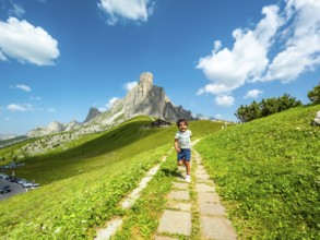 Happy child running on a path at giau pass in the italian dolomites with a mountain peak and blue