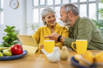 Mature couple exploring the net using digital tablet together at home while having breakfast