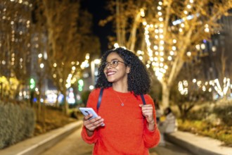 Smiling student walking in a decorated city using her smartphone during christmas holidays