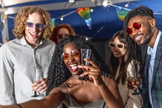 Multi-ethnic chic friends enjoying party at night and taking selfie together while raising
