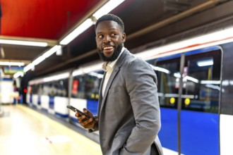 Young black businessman waiting for subway train while using his smartphone and looking away