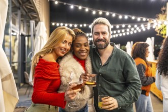 Multiracial happy friends smiling toasting at camera in a bar terrace at night