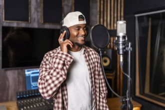 Young happy african american male singer wearing headphones and recording a song in professional