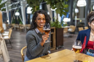 Latin woman enjoying beer talking to friends sitting on the terrace of a night bar