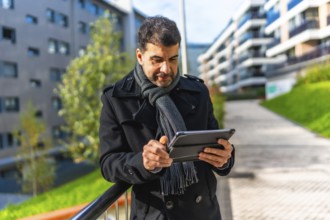 Businessman in casual winter clothes using digital tablet standing outdoors in the city in winter