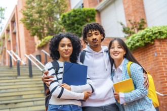 Portrait of three multi-ethnic university students embracing together standing in the campus