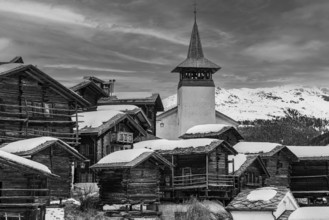 Old wooden houses with snow-covered roofs and the Saint Theodule church in the historic village