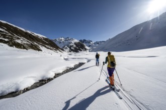 Two ski tourers in the snow by a mountain stream in the Funtauna Valley, Graubünden Haute Route,