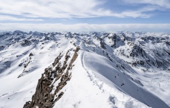 Tracks in the snow on a narrow mountain ridge in winter, summit of Piz Grialetsch, view of mountain