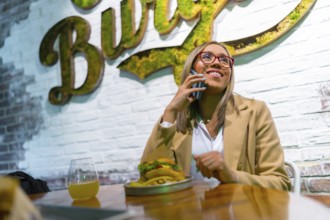 Stylish latin beauty blonde woman talking to the phone eating burger at restaurant