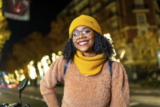 Portrait of a young woman wearing winter clothes and smiling in a city street decorated with