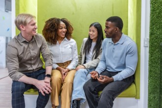Four smiling colleagues enjoying a relaxed conversation in a modern, green coworking office,