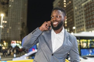 Young businessman smiling and chatting on a smartphone in a vibrant urban city at night, surrounded