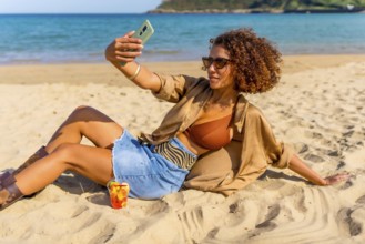 Confident woman in summer clothes taking selfie leaning on sandy beach