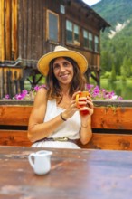Woman wearing a straw hat enjoying a hot beverage in a mountain chalet by the lake in the italian