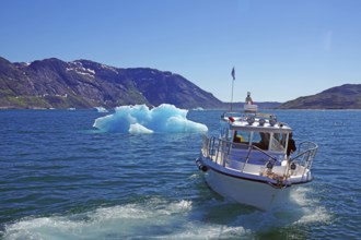Boat sailing on a blue sea with iceberg and mountains in the background under a sunny sky, small
