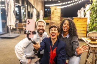 Caucasian adult female vlogger laughing with diverse friends celebrating night party and recording