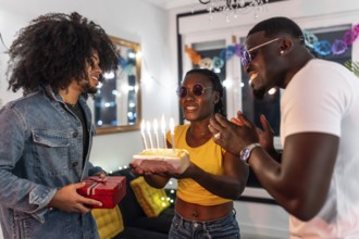Friends surprising latin man with birthday cake and present celebrating a party at home at night