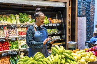 Young saleswoman using digital tablet and managing organic food in supermarket, she's wearing an