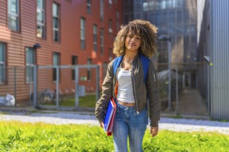 Beauty latin student standing outside the university smiling at camera and carrying folders,