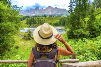 Female tourist with backpack and straw hat admiring the beautiful landscape of lake carezza and